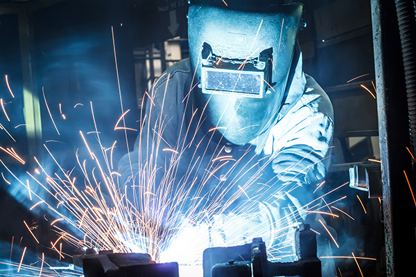 A welder wears a face shield while working on metal.