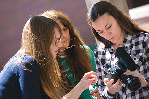 Three students examine a digital camera