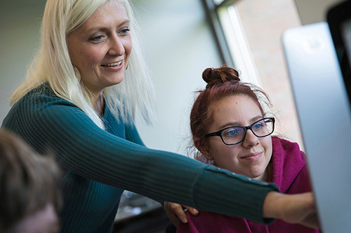 An instructor works with a student on a Mac