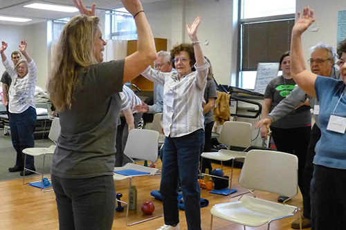 A physical therapy assistant demonstrates mobility exercises to a group of elderly patients