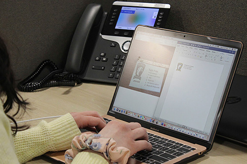 A student works on a laptop next to an office phone
