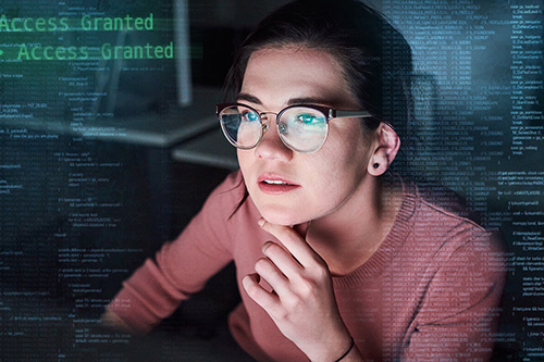 A female student leans in to inspect code on a computer screen