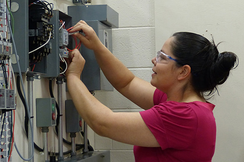 A female student works on a circuit breaker box