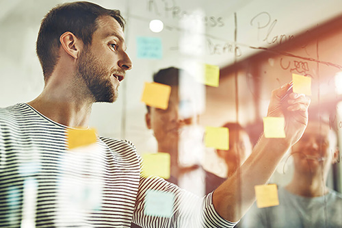 A project manager maps project requirements using post-it notes on a dry erase board