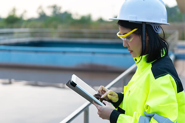 A woman wears a hard hat and safety glasses while inspecting wastewater facilities. 