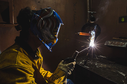 A student in a mask welds metal