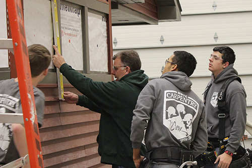 Four students measure siding for the outside of a shed