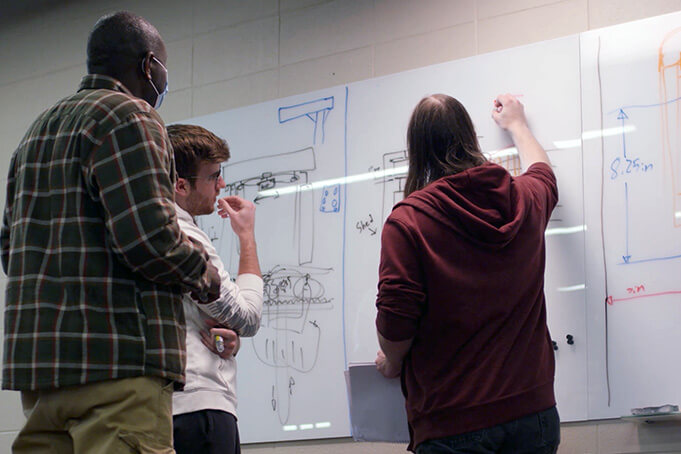 Students work together on the design of a mechanical part on a dry erase board