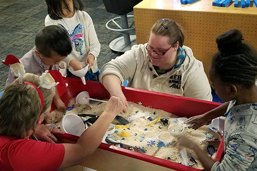 An early childcare worker plays with her students in the sand