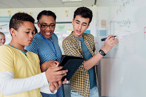 A teacher works with two students at a dry erase board