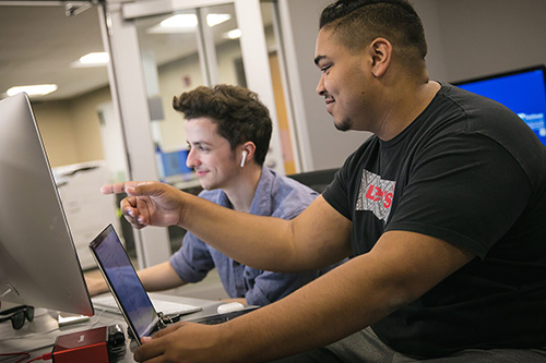 Two students work side by side in a computer lab