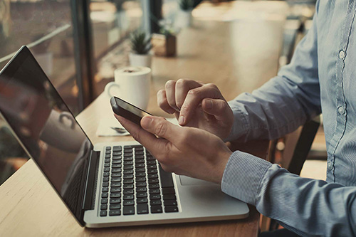 A man works on a laptop and phone in a coffee shop