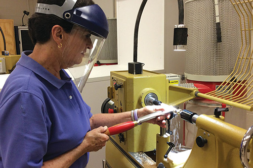 A woman turns wood on a lathe wearing protective gear