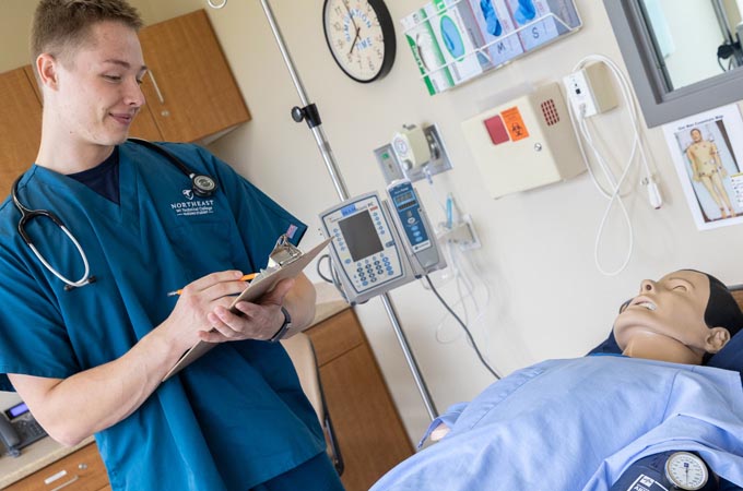 A student in scrubs works on a patient simulator