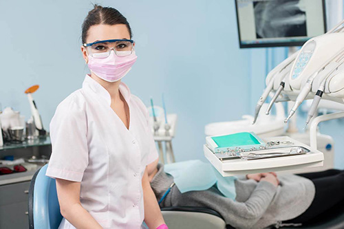 A dental hygienist sits next to a patient while wearing a face covering