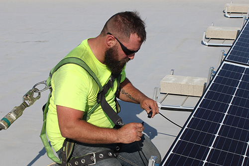 A student wearing a safety harness works on rooftop solar panels