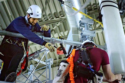 Two technicians atop a cellular tower adjusting cables