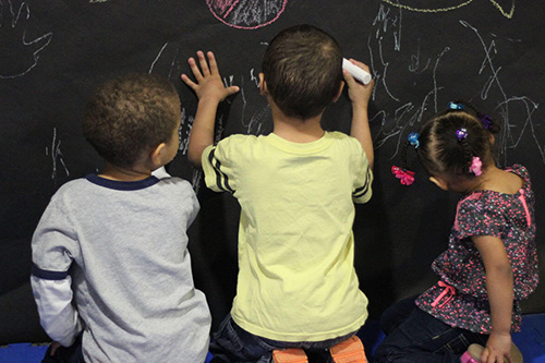 Three children draw on a chalkboard