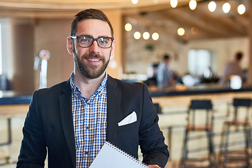 A restaurant manager stands in front of the bar area of a restaurant