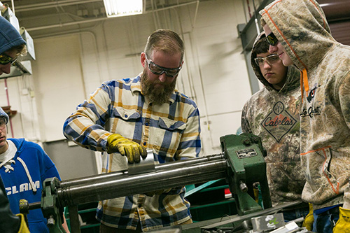 Students watch an instructor fabricate a part on a machine