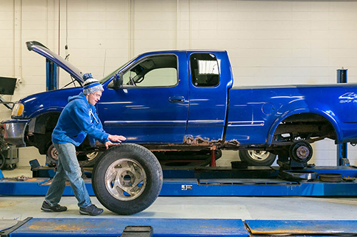 A student puts tires on a truck on a lift.