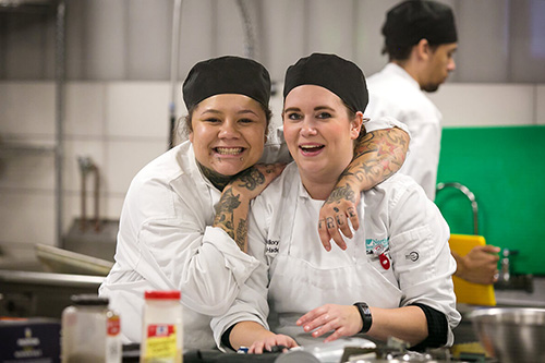 Students smile at the camera in the culinary lab