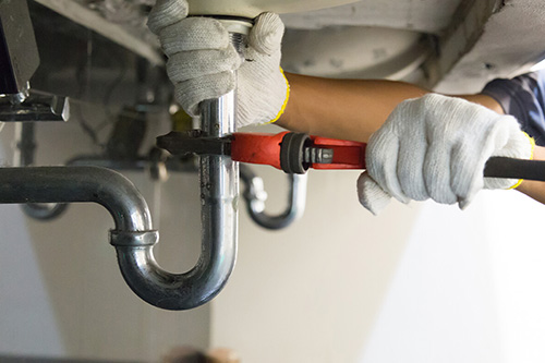 A plumber adjusts the piping below a sink