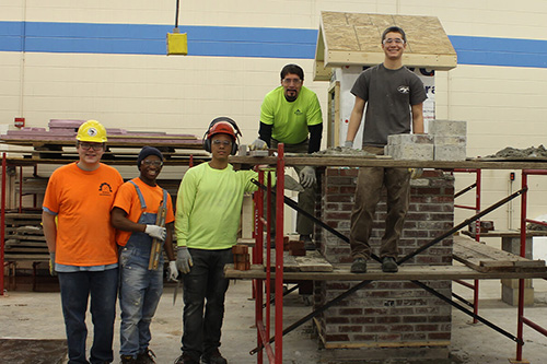 Masonry students stand near a chimney they built