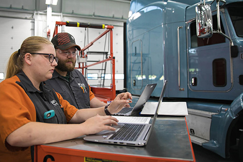 Students work on laptops running diagnostics on a semi truck