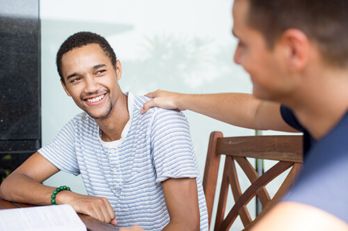 A man comforts another man sitting at a table