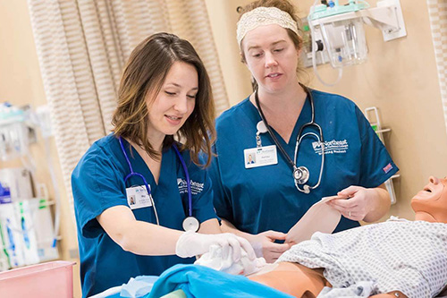 Two student nurses in scrubs work on a patient simulator