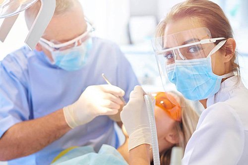 A dental assistant works on a patient's teeth while wearing a face covering 