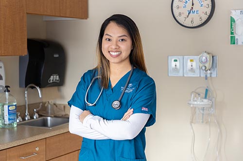 A female nurse in scrubs stands in a patient's room