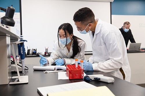 Two students work together wearing masks in the lab