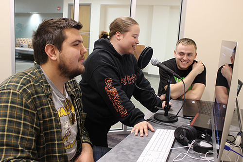Students record another student talking and edit the audio files on a computer