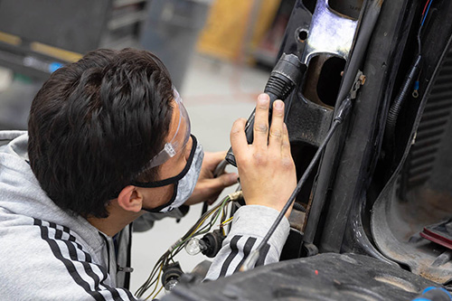 A student wearing a mask works on a car