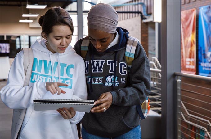 Two students review notes on a notepad in the hallway outside a classroom