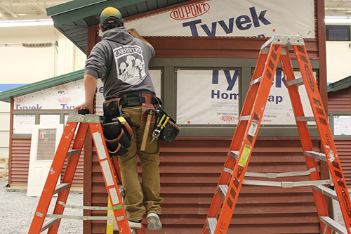 A student works on siding on a ladder