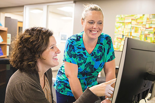 A nurse and an administrator work together on a computer