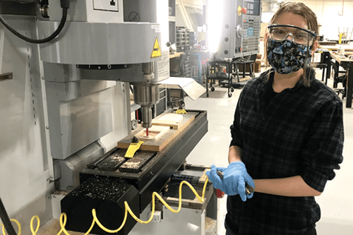A Prototype and Design student wears a mask in front of a fabricating machine.