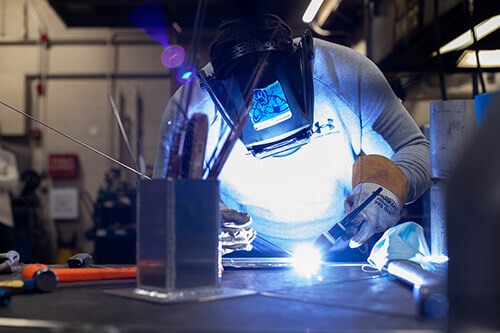A student wearing a protective mask welds metal
