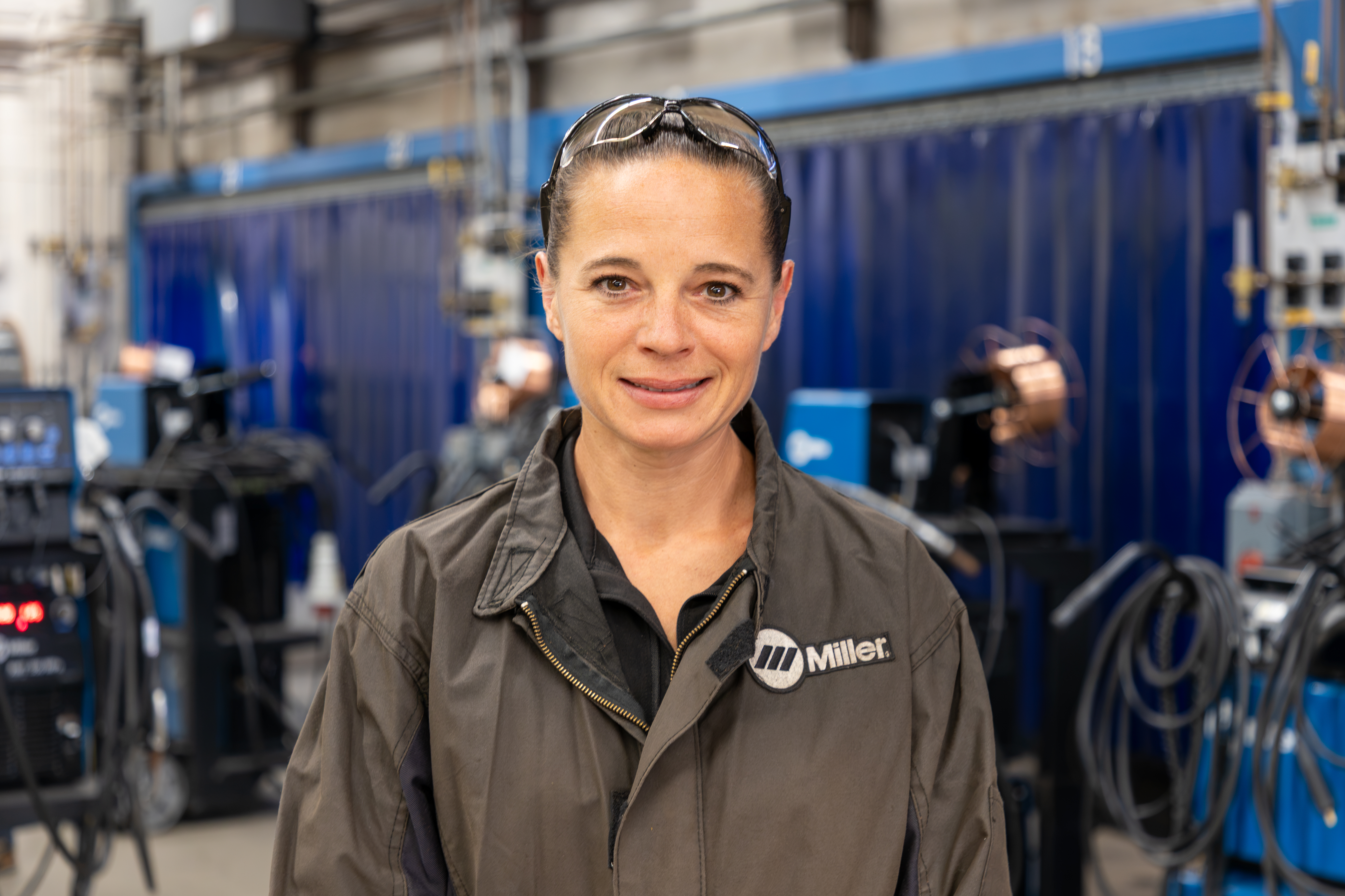 Sarah Fischer, standing in welding lab, faces camera, smiling