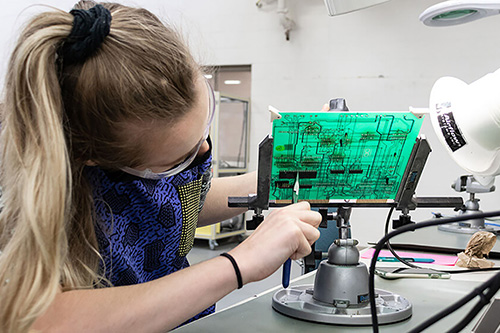 A student wearing protective eyewear works on electronic devices