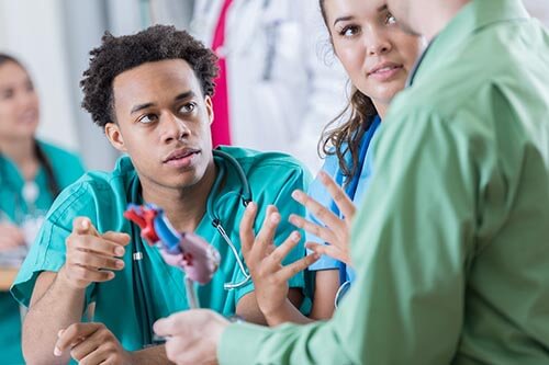 Students wearing scrubs looking at model of a heart