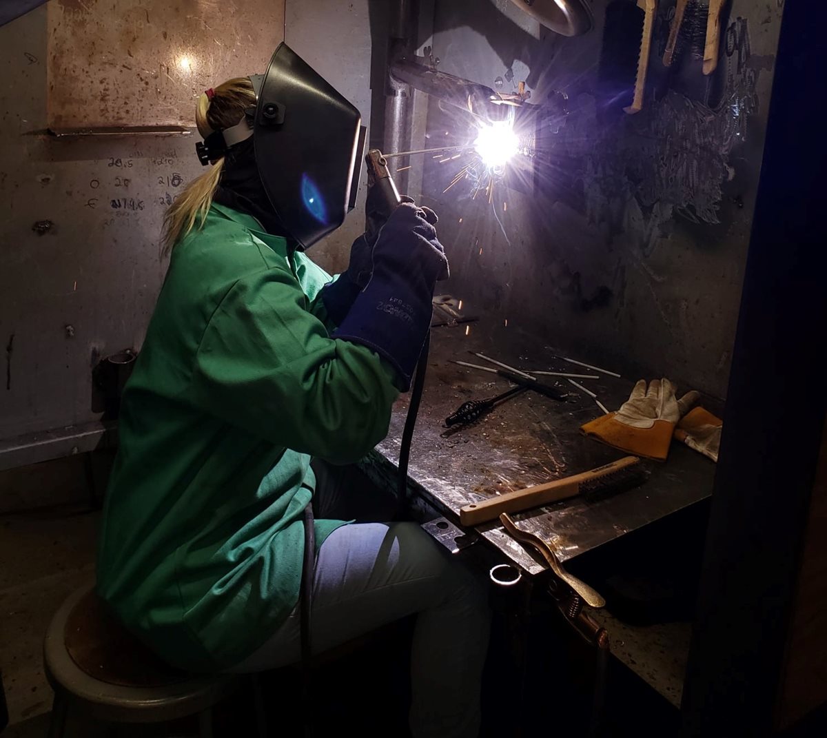A female student welds metal wearing protective gear. 