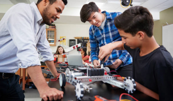 A teacher works with high school students to create a remote controlled vehicle