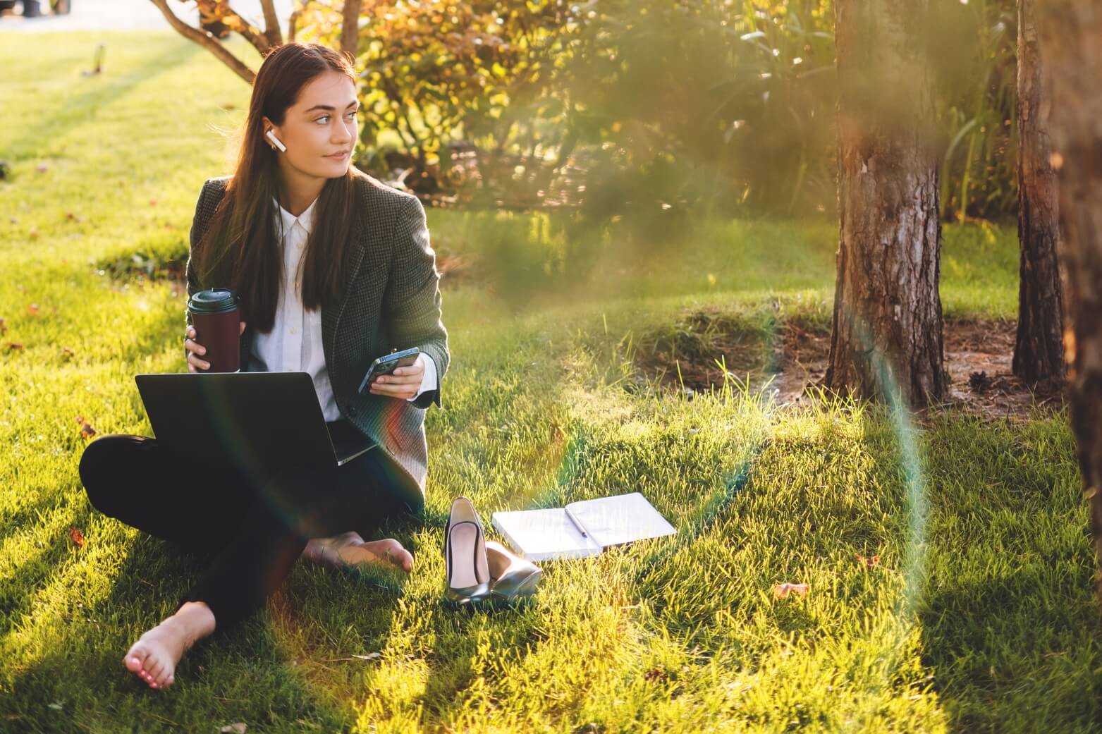 Woman in a suit sitting out in field working on computer 