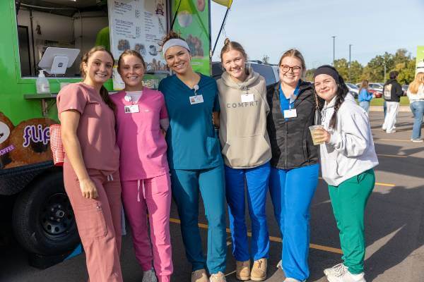 Group of six nursing students in scrubs pose for picture, outside at Fall Fest