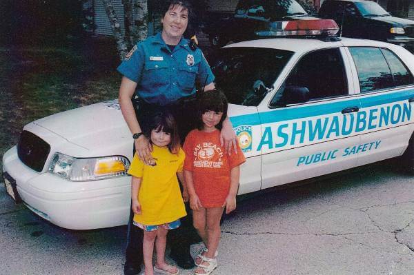 Diana Lawler standing with her young daughters in front of an Ashwaubenon Public Safety squad car
