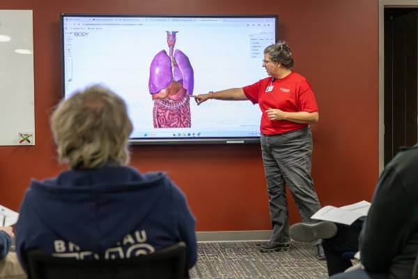 Diana Lawler stands in front of classroom, pointing at human anatomy image